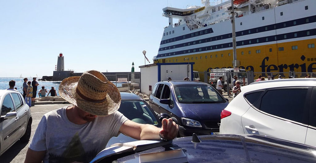 Une famille avec bagages et poussette attendant dans une zone d'embarquement d'un port corse